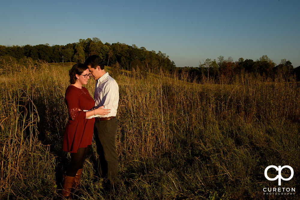 Future bride and groom standing in a field during their engagement session.