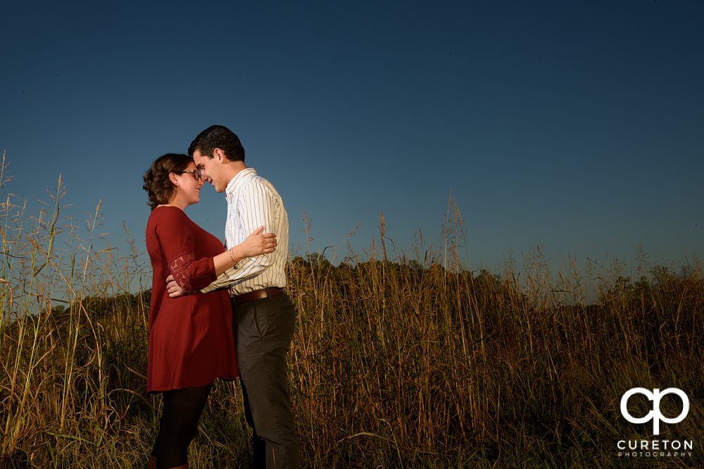 Bride and groom hugging during their engagement session in the middle of the field.