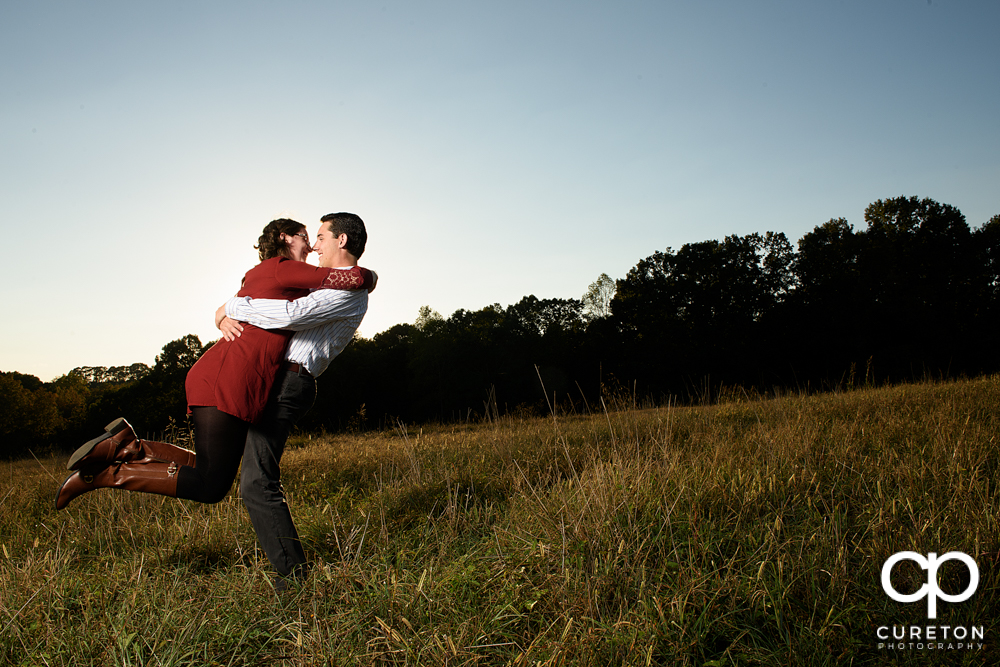 Groom lifting his bride in a field during their engagement session.