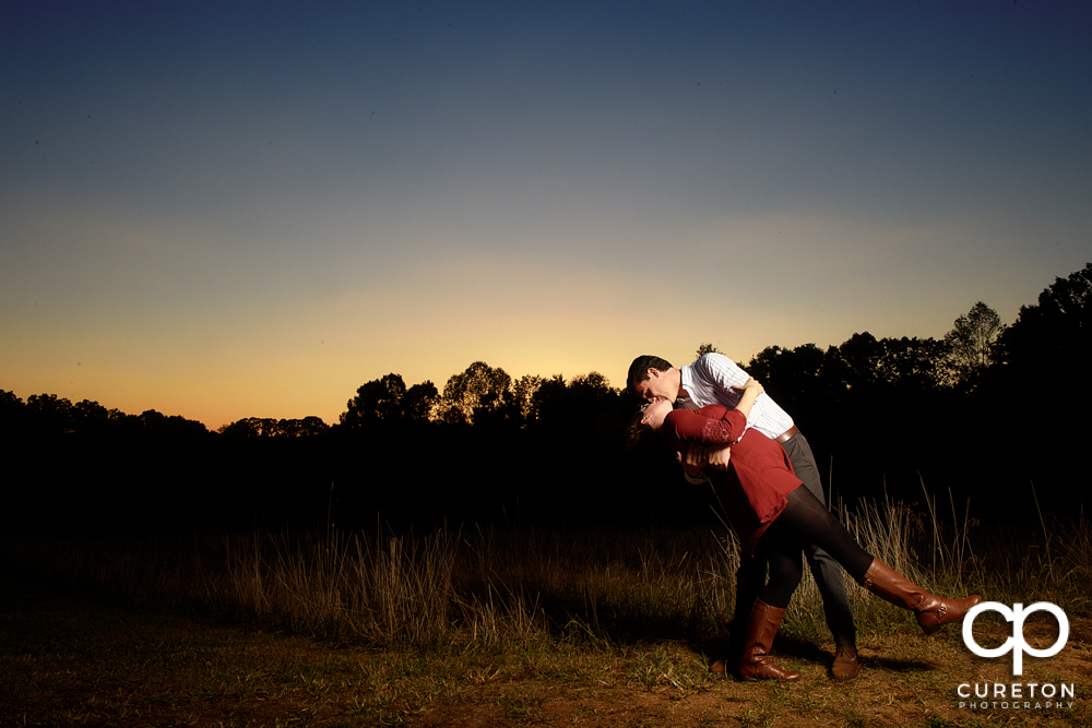 Man dipping his fiancée at sunset during their engagement session.