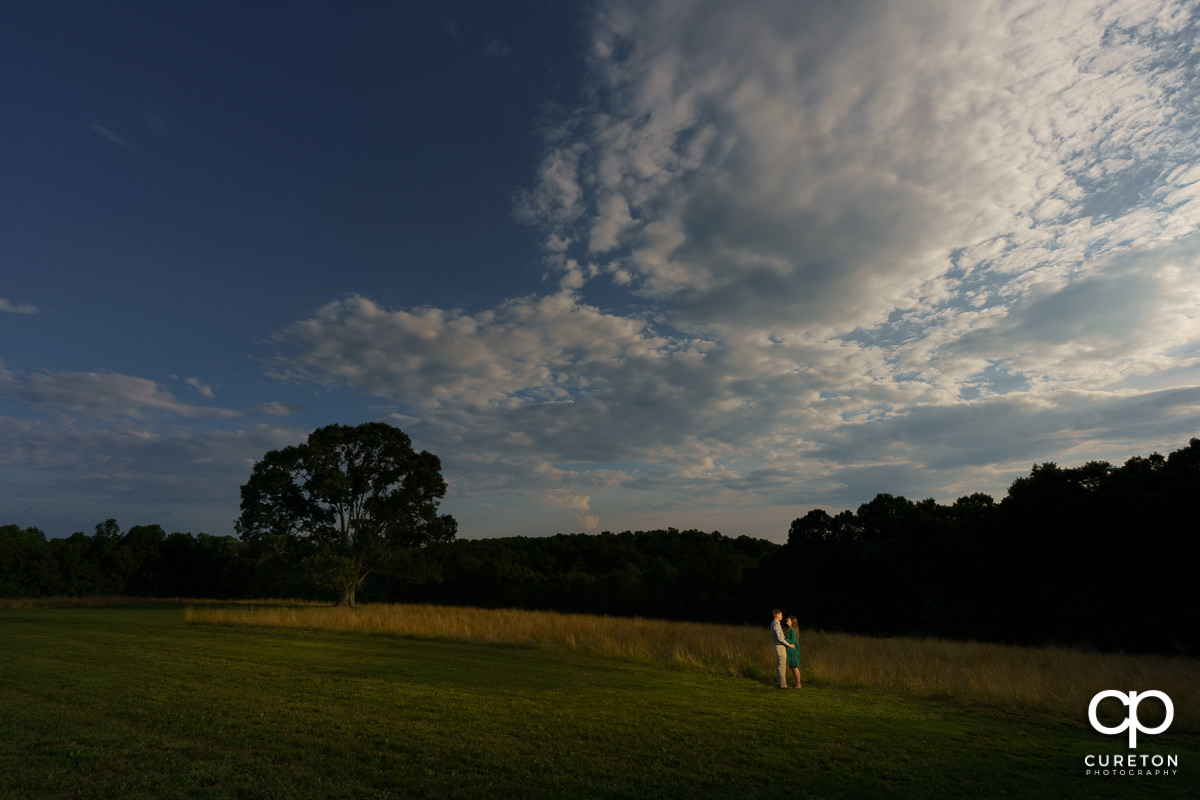 Bride and groom in an open field near a huge oak tree during their engagement session at Greenbrier Farms in Easley,SC.