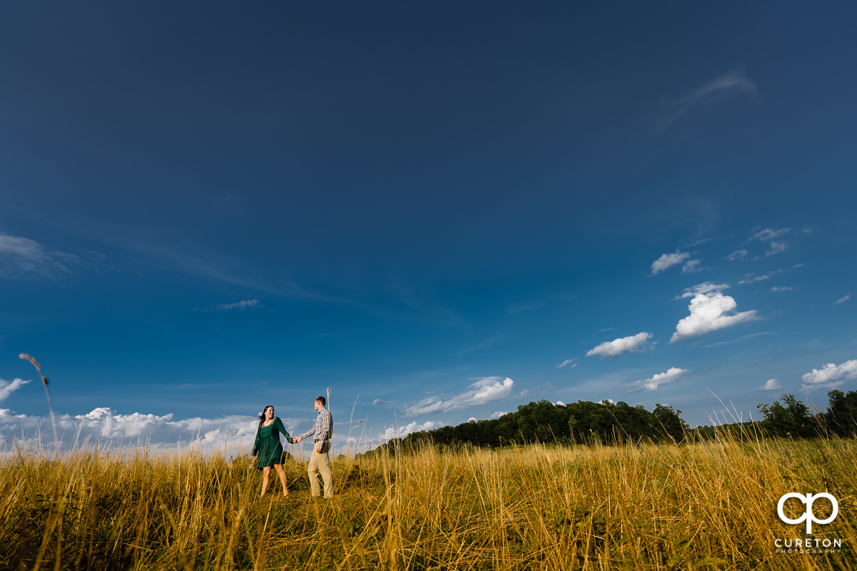Engaged couple walking in a field during their engagement session at Greenbrier Farms in Easley,SC.