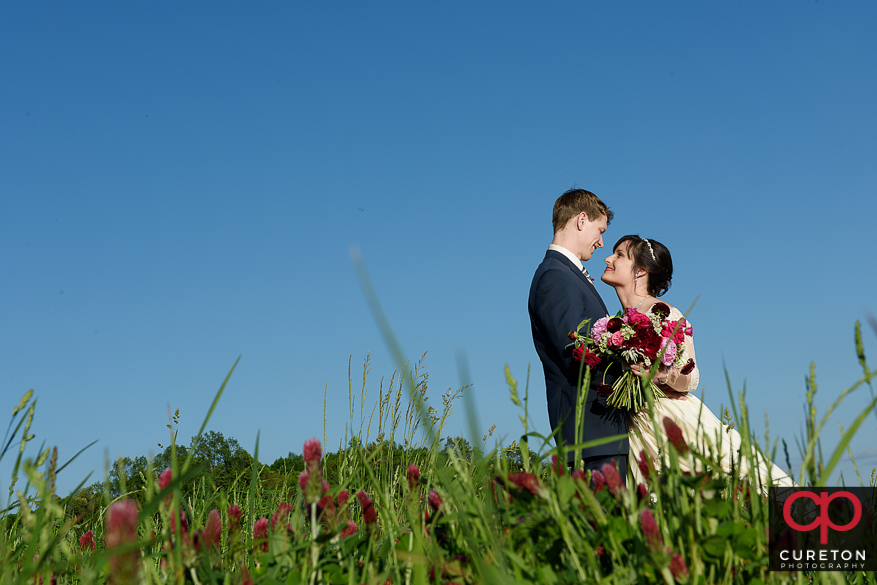 Bride and groom standing in a patch of clover at a rustic farm wedding. 