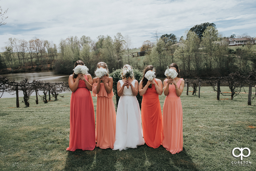 Bride and the bridesmaids with flowers in front of their faces.