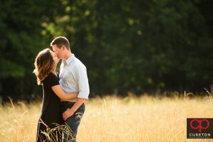 Future bride and groom kissing in a field of tall grass.