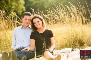 Engaged couple sitting in a field of tall grass.