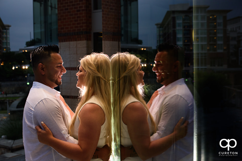 Couple smiling in their reflection during an engagement session in downtown Greenville,SC.