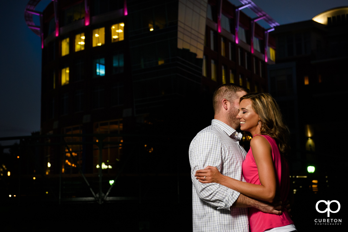 Engagement photo of a couple dancing with the downtown Greenville skyline in the background.