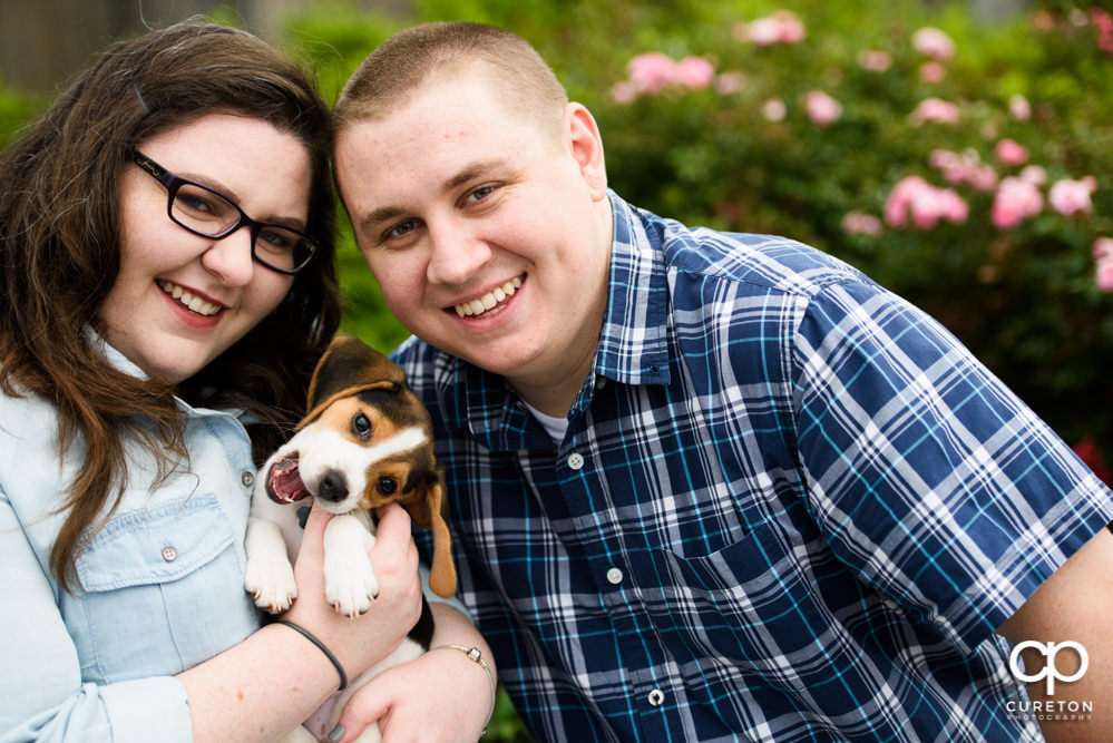 Couple smiling with a beagle during their engagement session with their puppy in downtown Greenville.