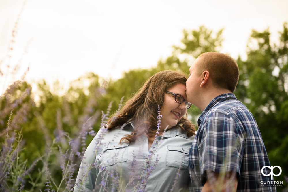 Man kissing his fiancee on the forehead during their engagement session with their puppy.