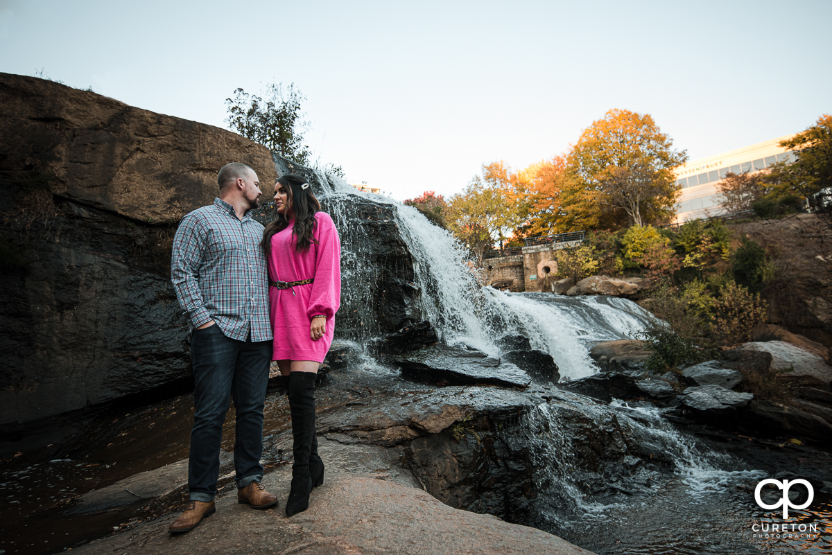 Man and woman standing on a rock in the middle of the Reedy River during a Falls Park engagement in downtown Greenville,SC.