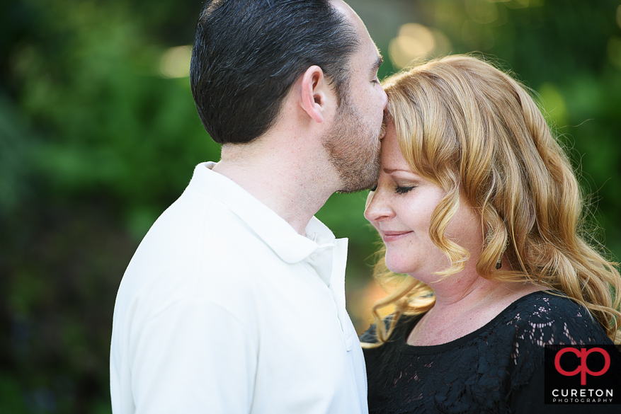 A man kissing his fiancee on the forehead during a falls park engagement session.