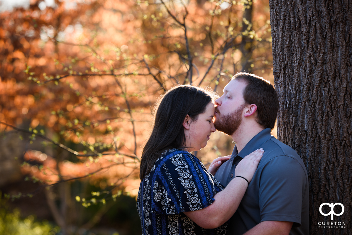 Man kissing his fiancee on the forehead during a Greenville,SC park engagement session.