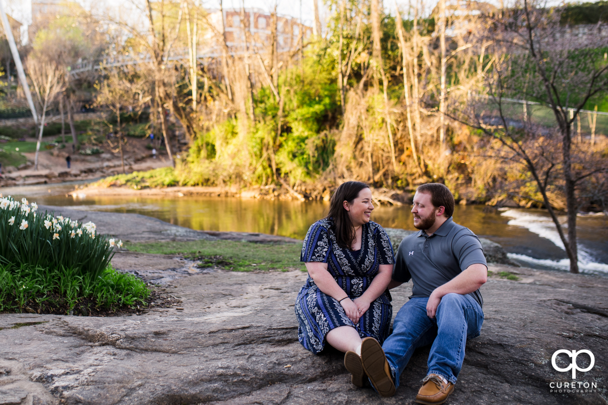 Engaged couple sitting on a rock near the Reedy river.