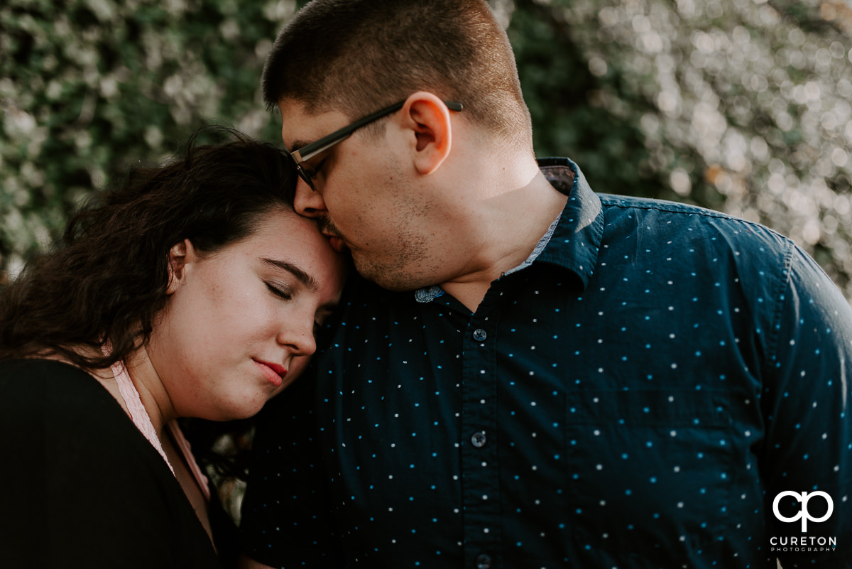 Man kissing his fiancee on the forehead during a spring engagement session in downtown Greenville ,SC.