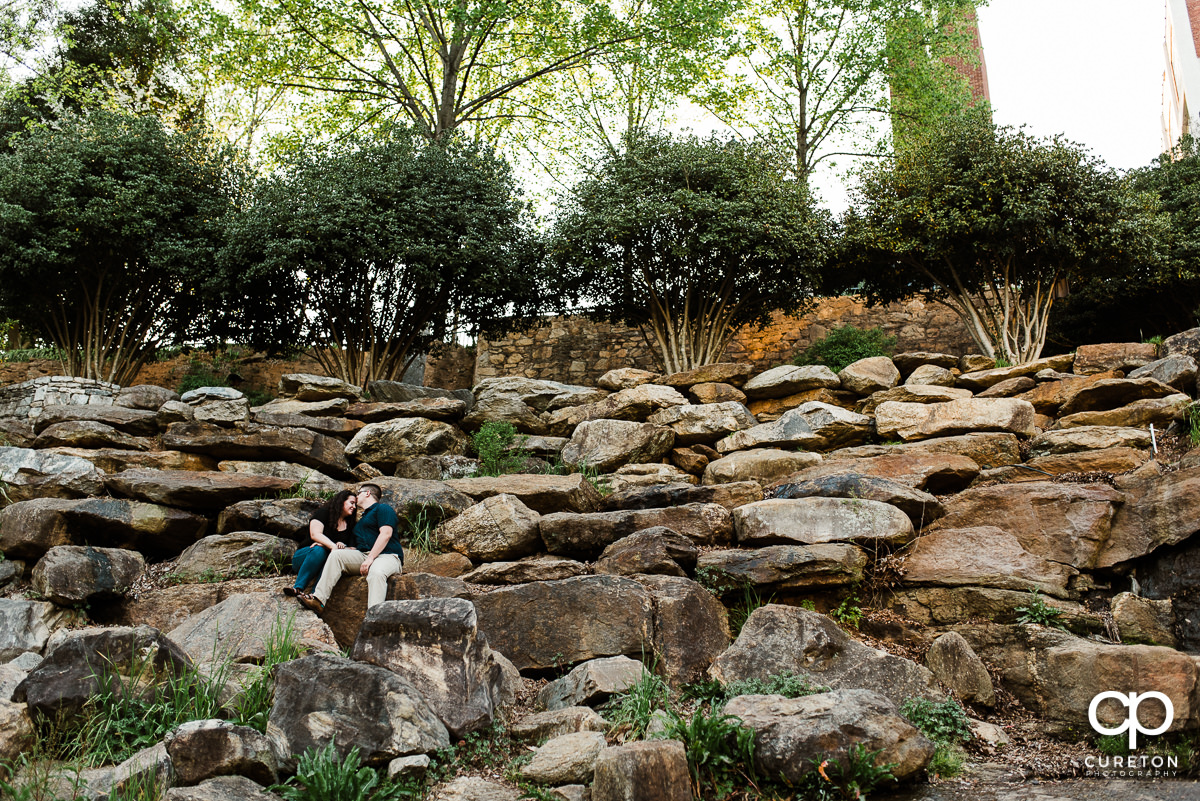 Bride and her future groom sitting on the rocks in Falls Park spring engagement session in downtown Greenville,SC.