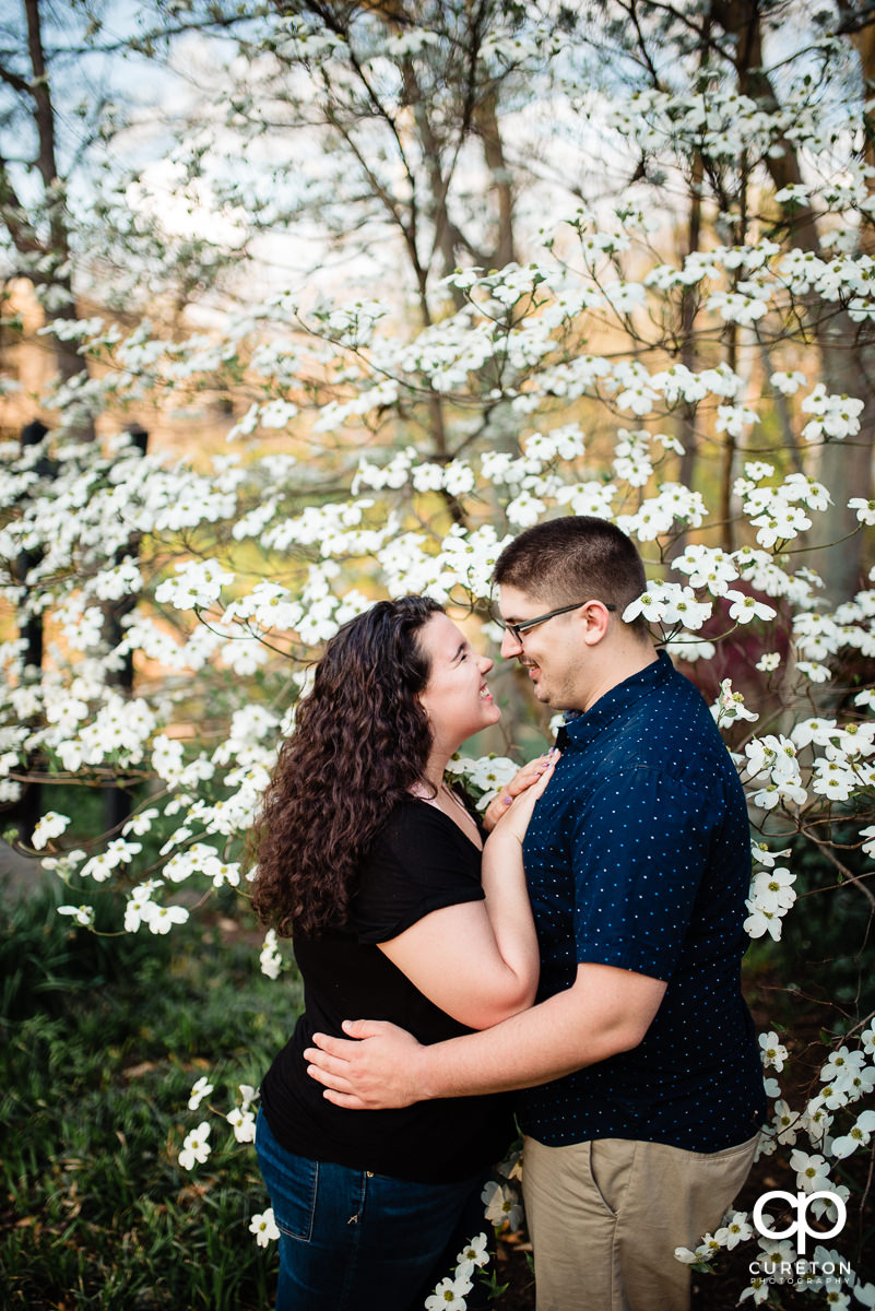 Future bride and groom standing in some flowers in Falls PArk spring engagement session in downtown Greenville ,SC..