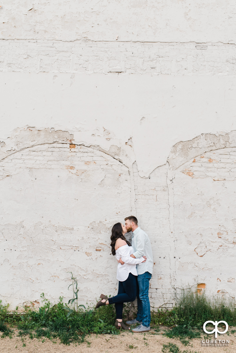 Man kissing his wife while dancing in front of a white wall during a Greenville,SC anniversary session.