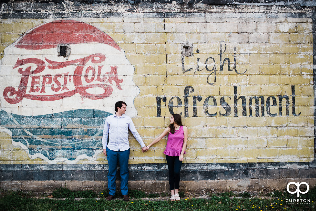 Engaged couple gazing at each other in front of a vintage painted wall.