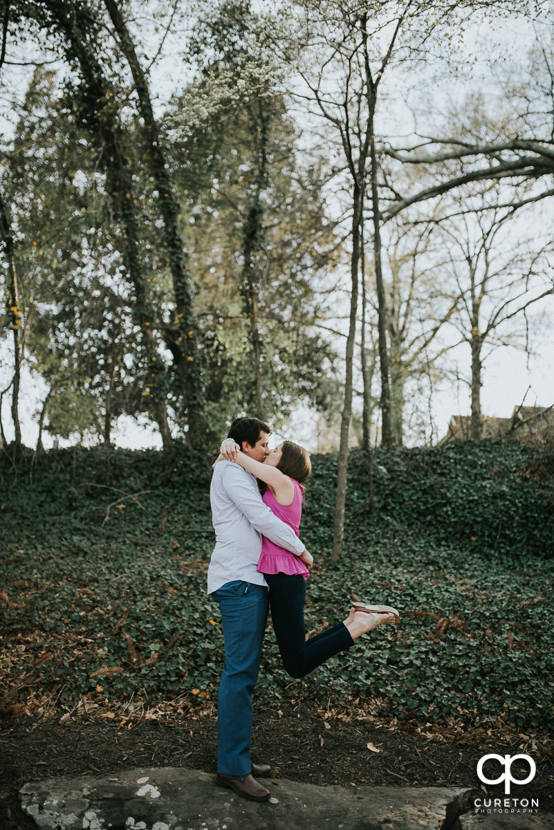Man lifting his future bride and kissing her at their engagement session.