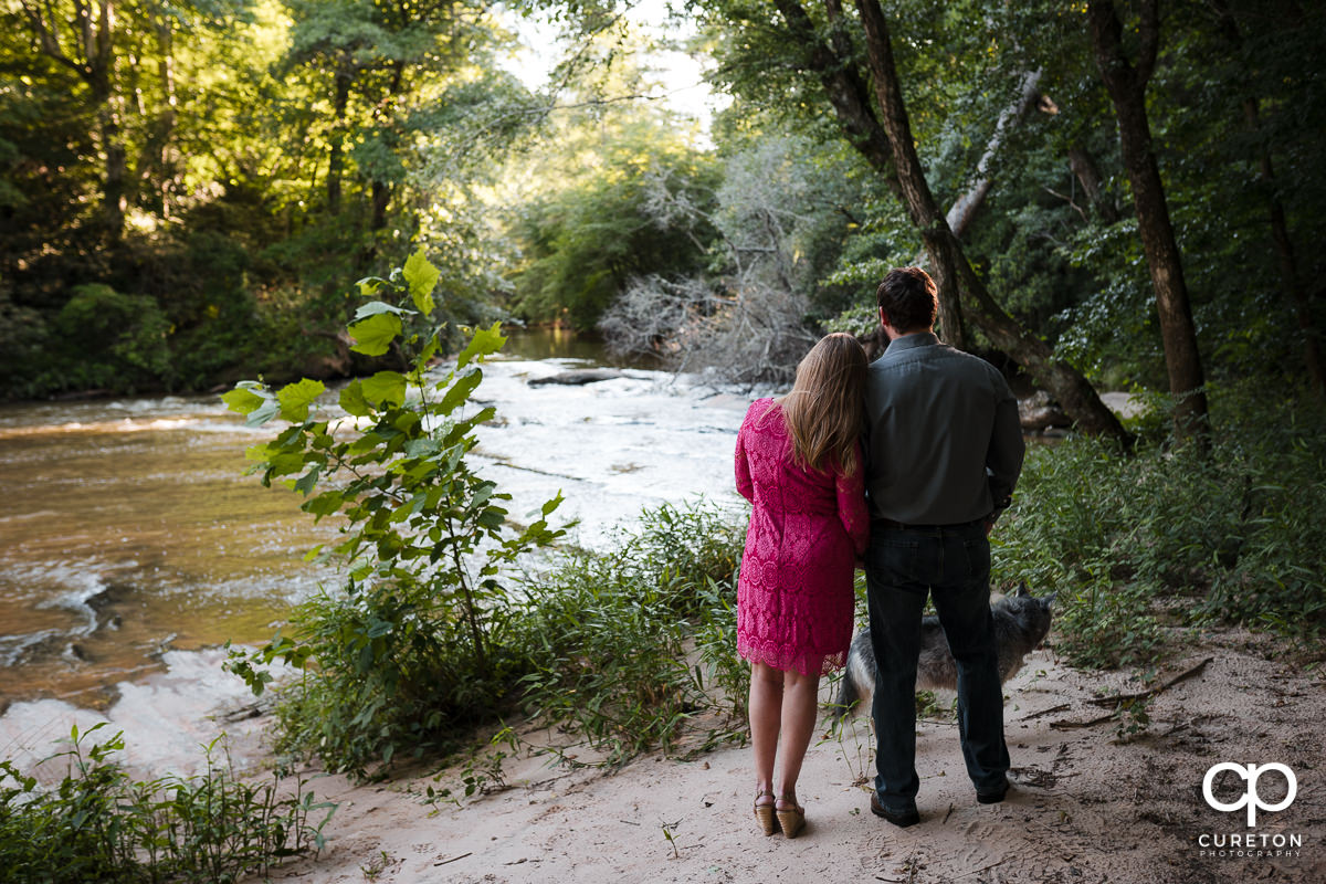 Engaged couple and their dog looking out at the river.