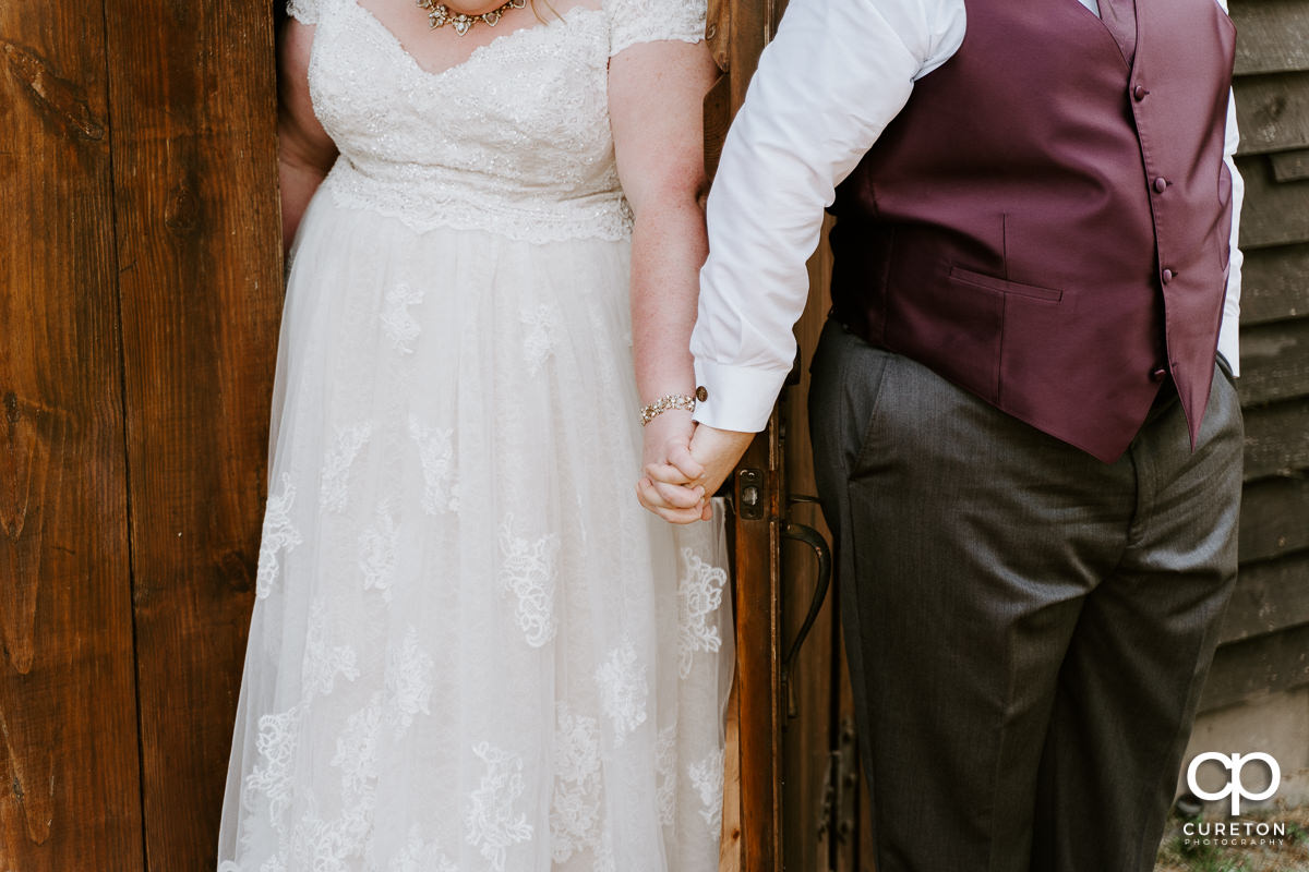 Bride and groom holding hands on the opposite sides of a door.