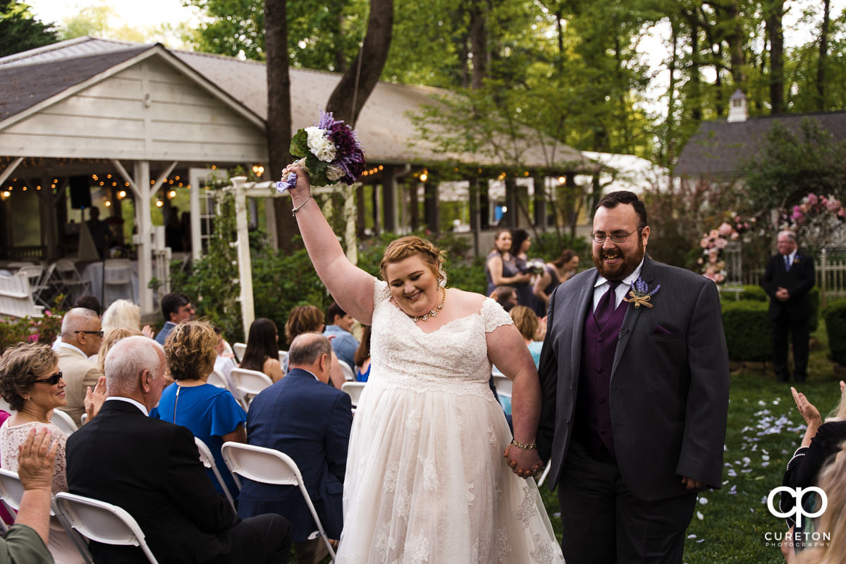 Bride holding her arm in the air as they walk back down the aisle at the Grove at Pennington wedding.