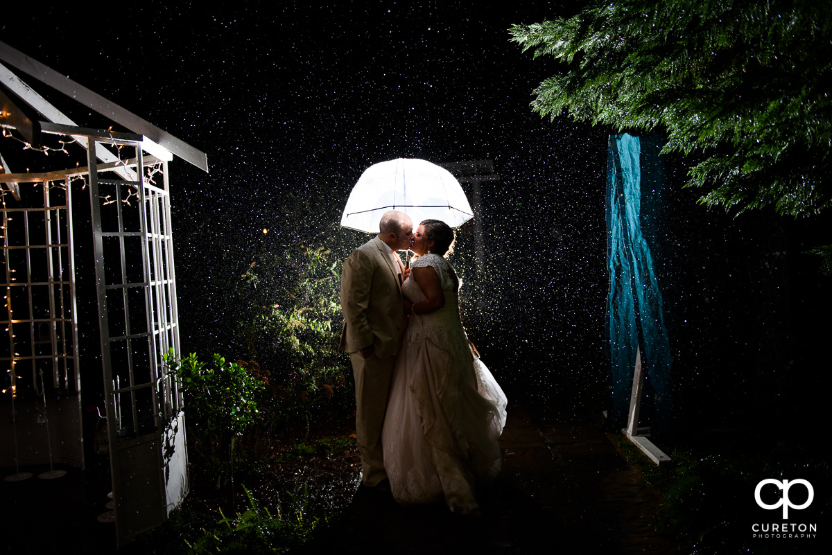 Bride and groom kissing underneath an umbrella in the rain after their Grove at Pennington wedding.