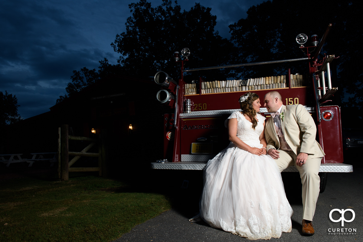 Bride and groom sitting on the rear deck of a fire truck.
