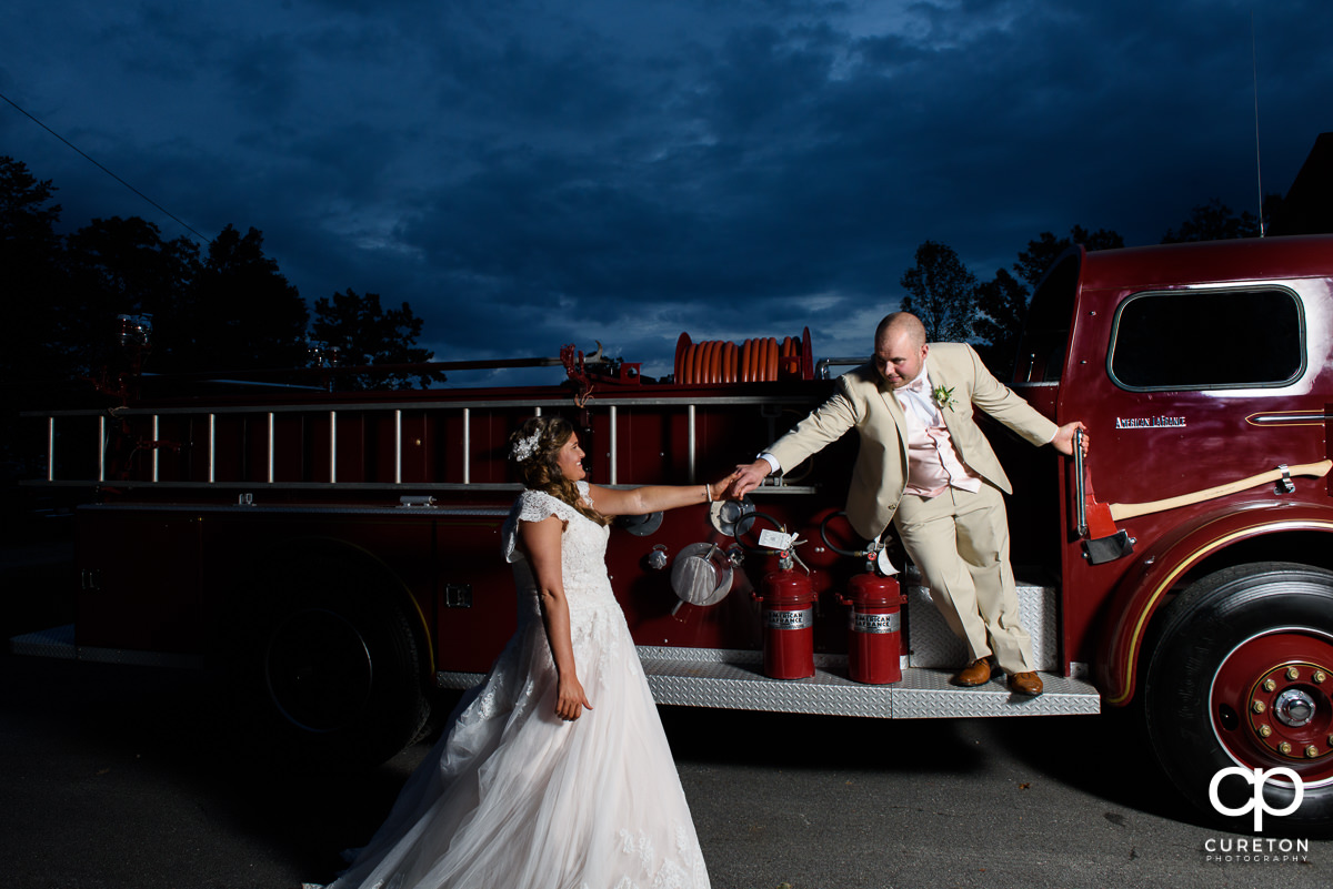 Groom reaching out to his bride while on a fire truck.