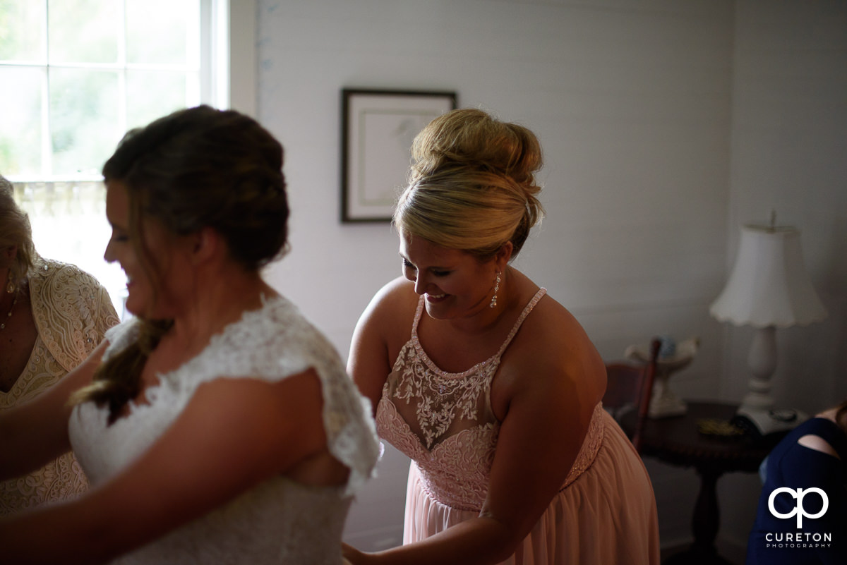 Brides sister zipping the back of her dress.