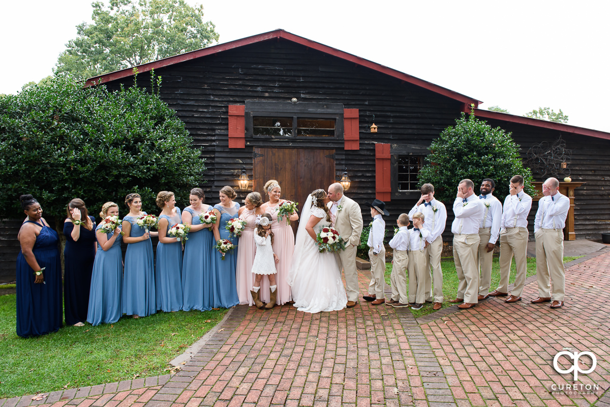 Wedding party looking away as the bride and groom kiss.