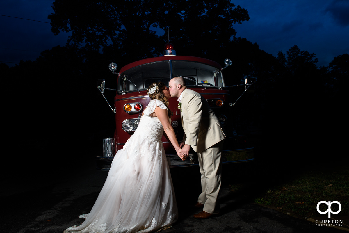 Bride and groom kissing in front of a fire truck.