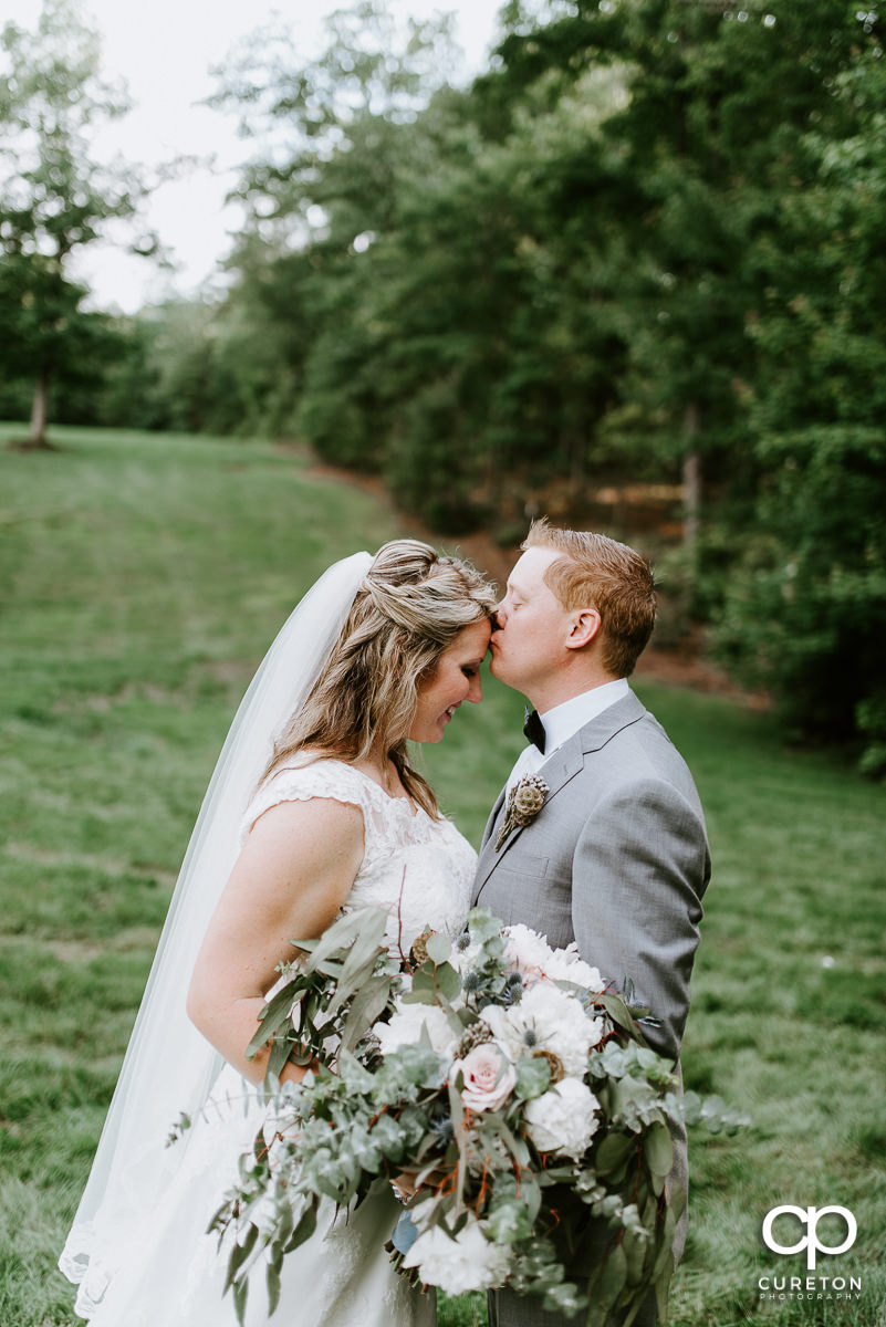 Groom kissing his bride on the forehead after their wedding ceremony at The Hollow at Paris Mountain.