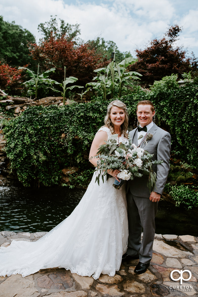 Bride and groom standing near a pond at The Hollow at Paris Mountain.