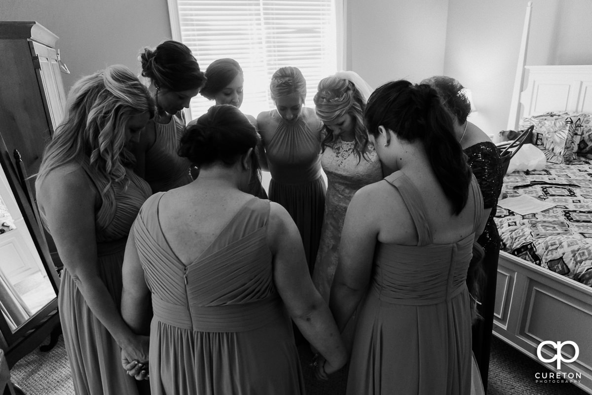Bride praying with her bridesmaids.