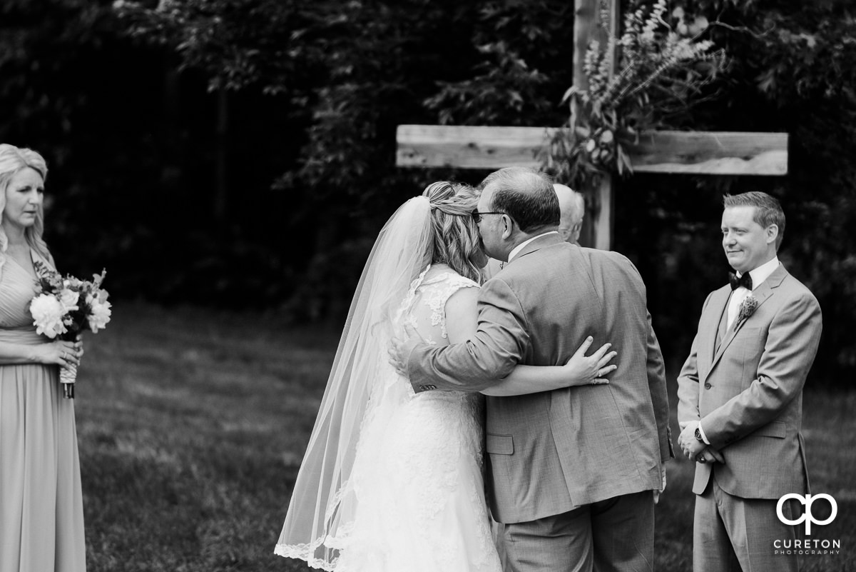 Bride's father kissing her on the cheek at the wedding ceremony.