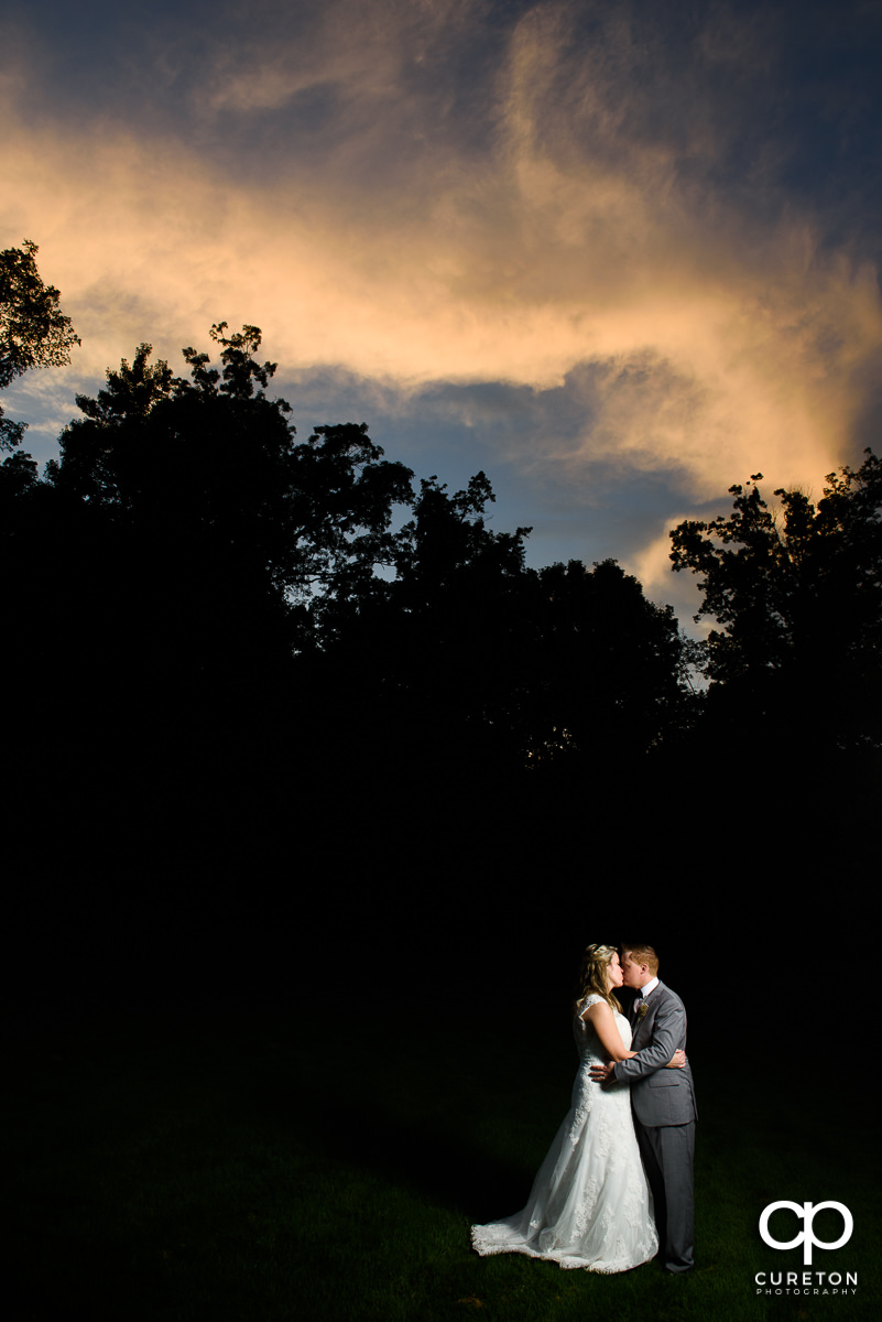 Bride and groom kissing under an amazing sunset at their wedding reception at The Hollow at Paris Mountain.