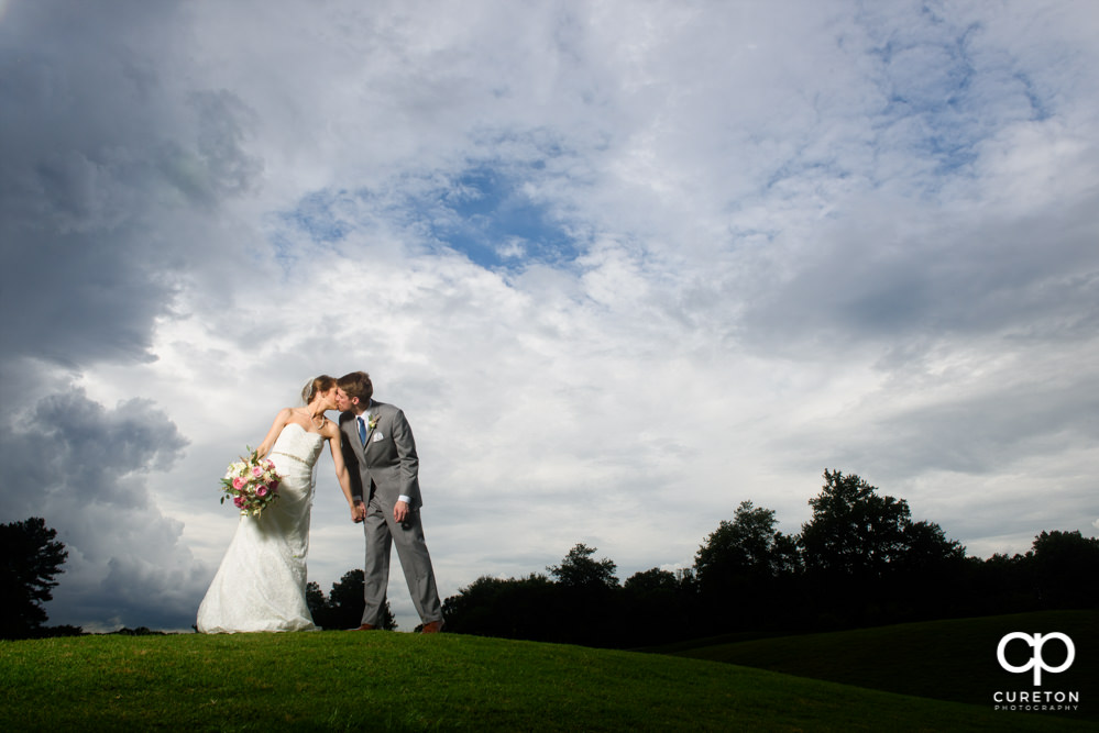 Bride and groom kissing on the golf course at Holly Tree Country Club.