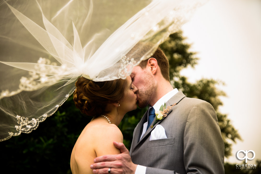 Bride and Groom kissing with her veil blowing in the wind at their Holly Tree Country Club wedding in Simpsonville SC.
