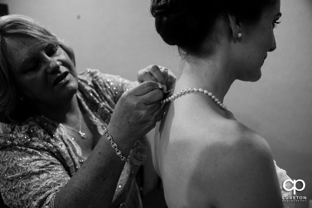 Bride's mom helping bride with jewelry.