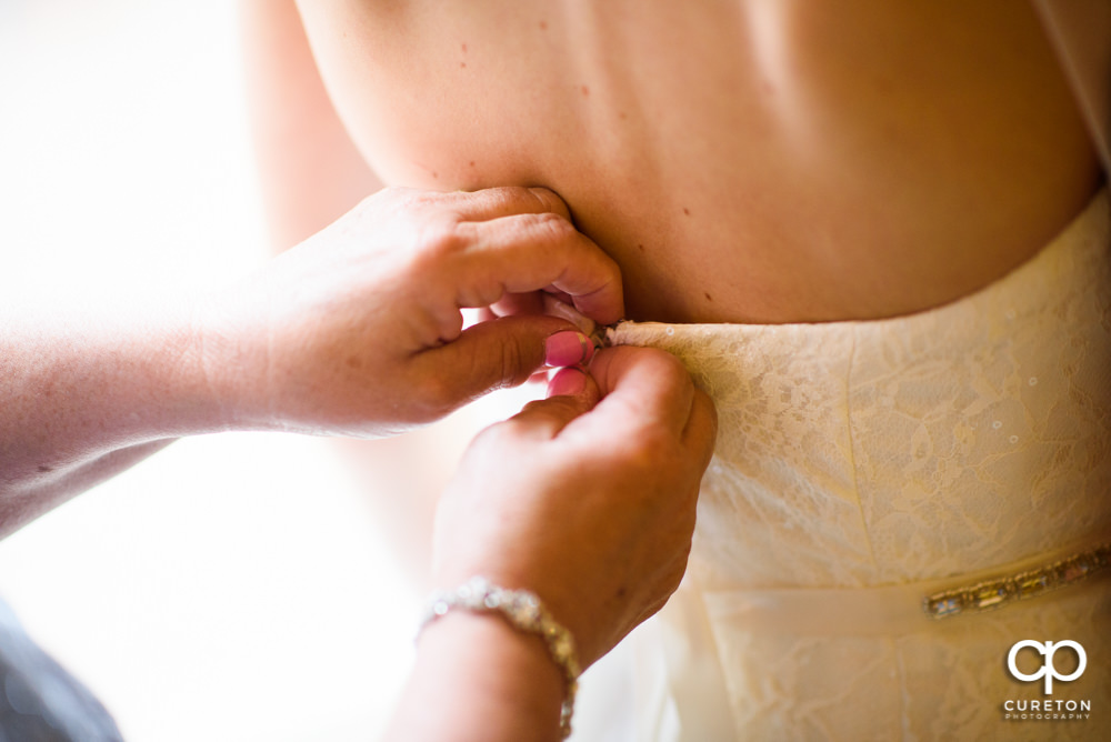 Bride's mom fastening the back of the dress.