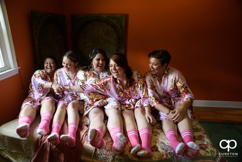 Bride and bridesmaids sitting on the bed laughing.