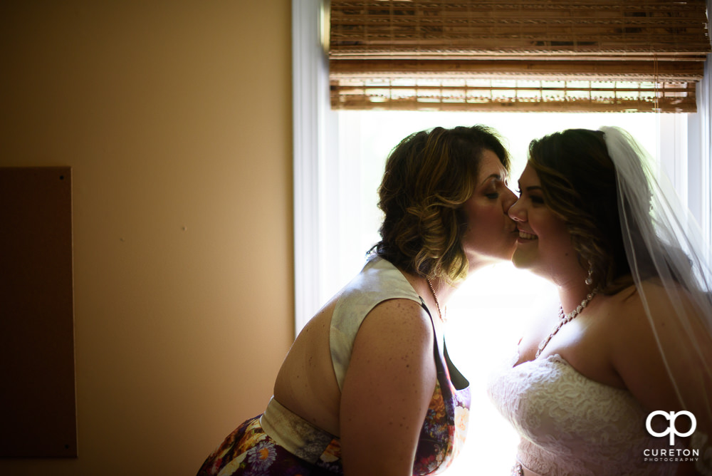 Bride's mom kissing her daughter on the cheek.