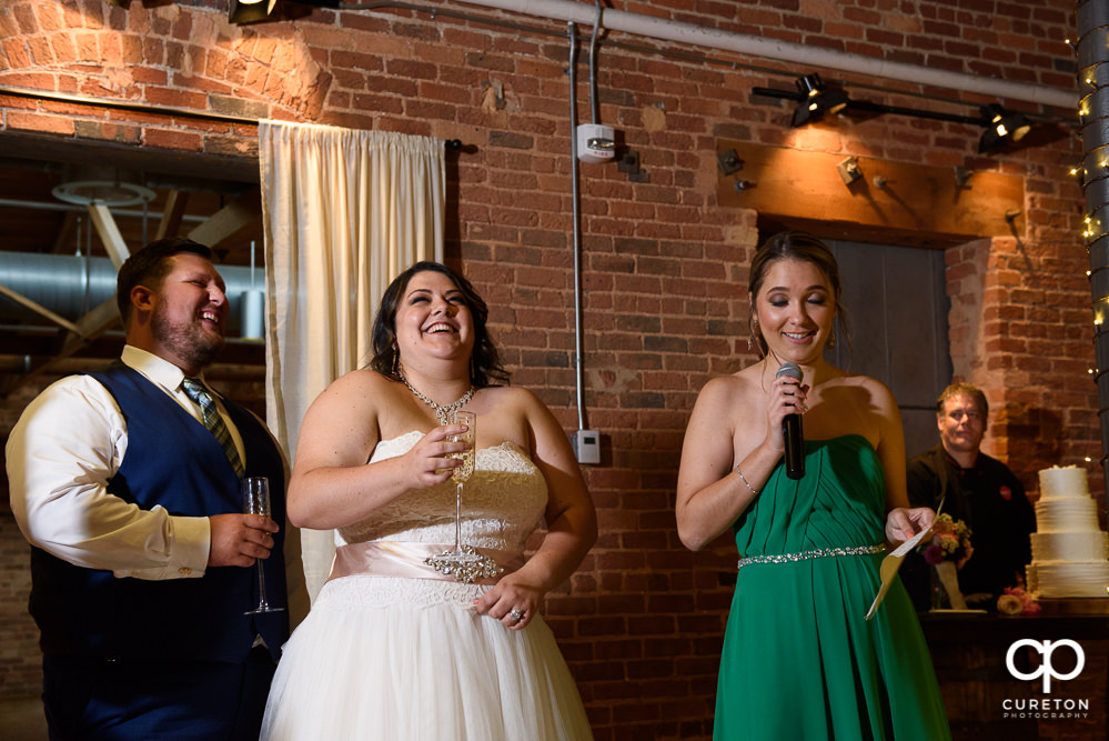 Bride and groom look on as the best man and maid of honor give toasts.