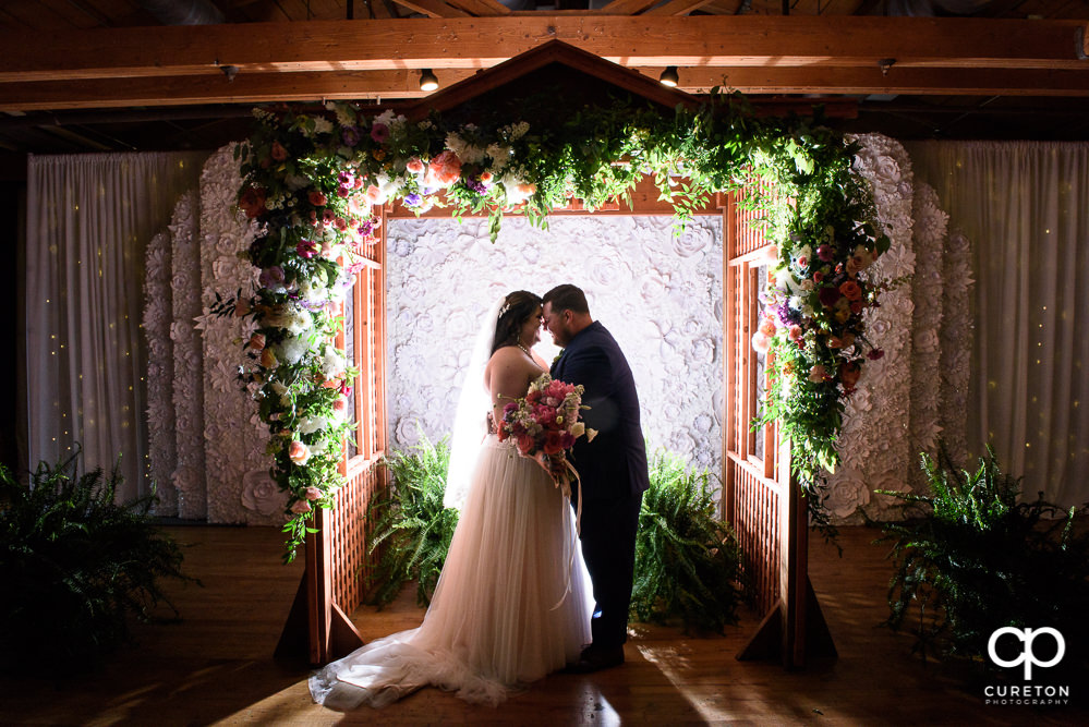 Bride and groom with a custom floral arbor at their Huguenot Loft wedding in Greenville SC.