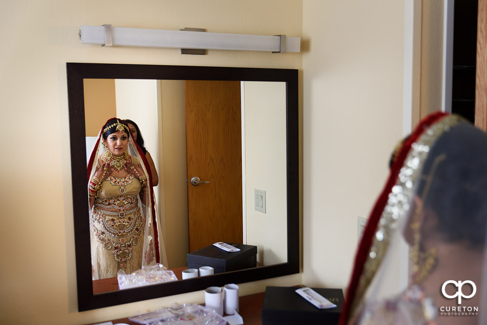 Indian bride getting ready for her wedding looking in the mirror.