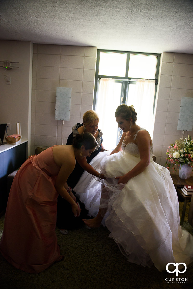 Bridesmaids helping the bride into her shoes.