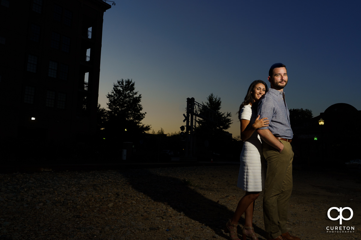 Man and his fiancee in front of some railroad tracks at sunset.