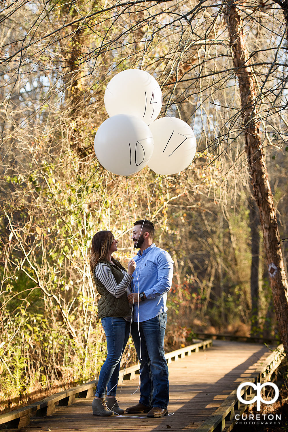 Engaged couple holding balloons with their wedding date on them.